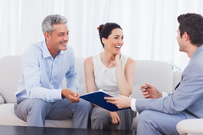 Salesman and clients talking and laughing together on sofa in home